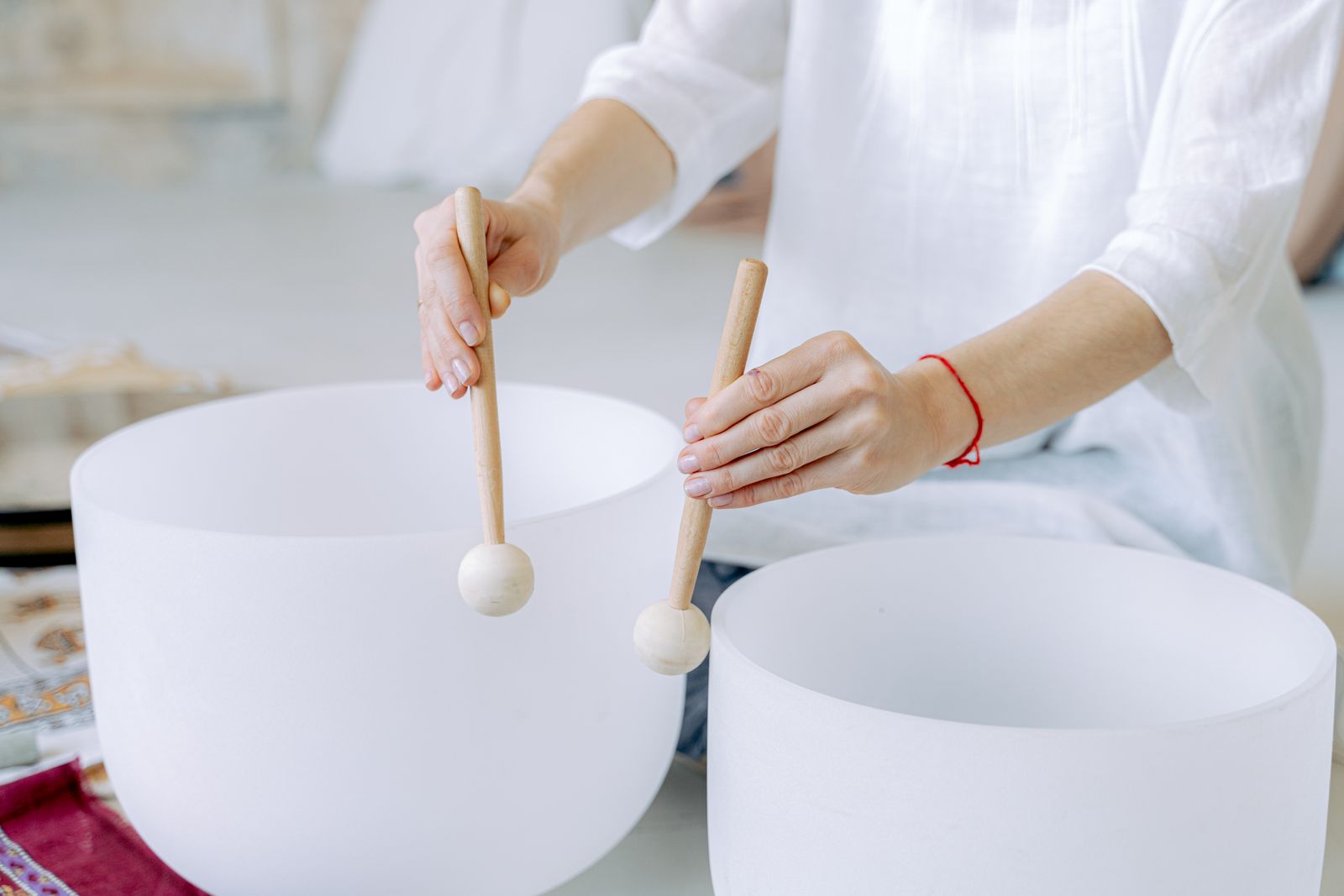 Two hands holding wooden mallets over a pair of frosted crystal singing bowls.